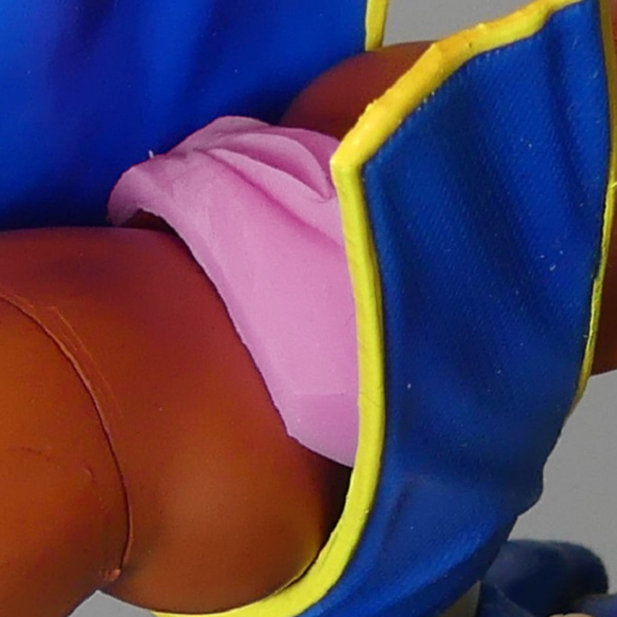 Close-up of a chun li doll wearing a blue outfit with yellow trim and a pink vagina, shown against a plain light gray background.