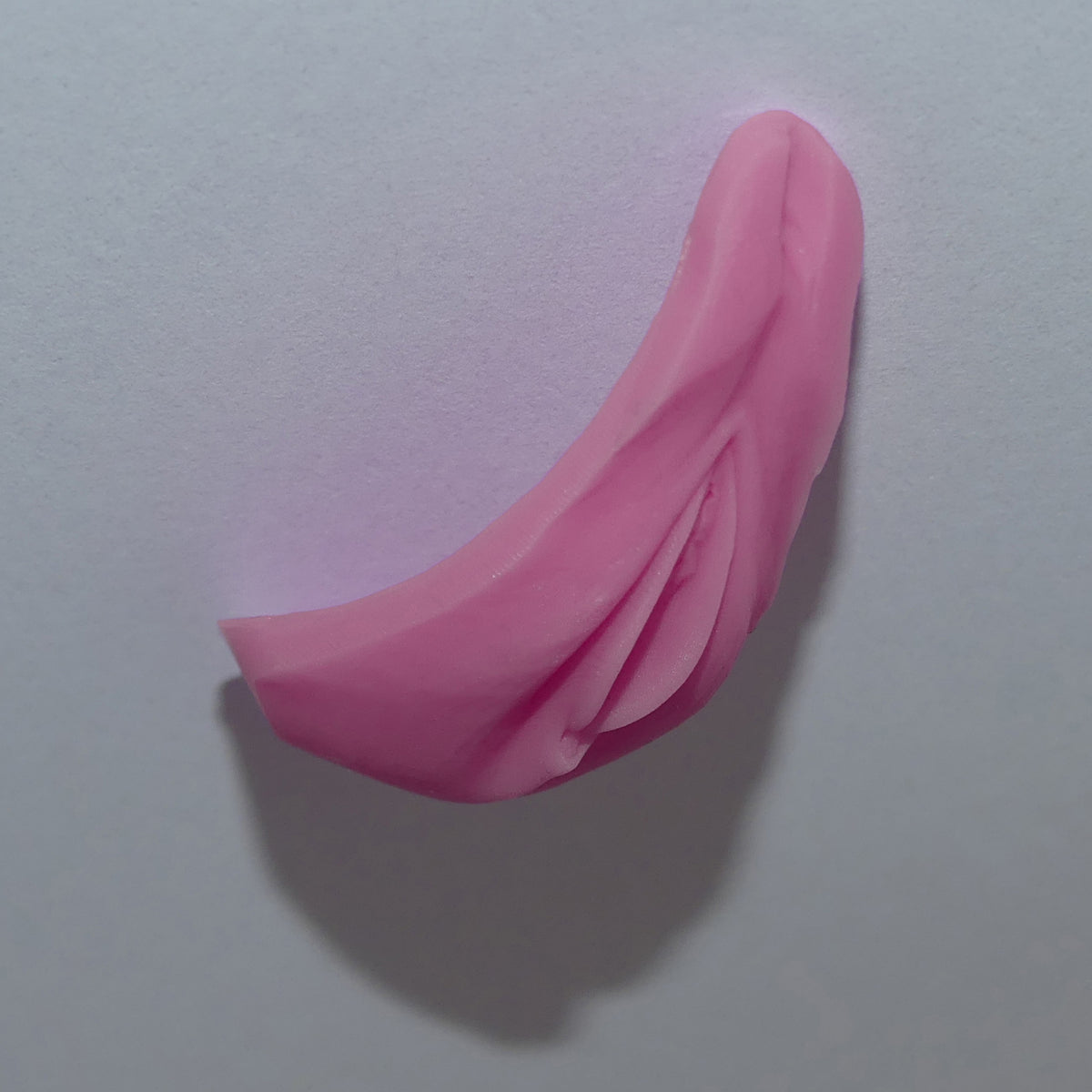 A pink silicone Barbie Vagina shown from the side against a plain light gray background.