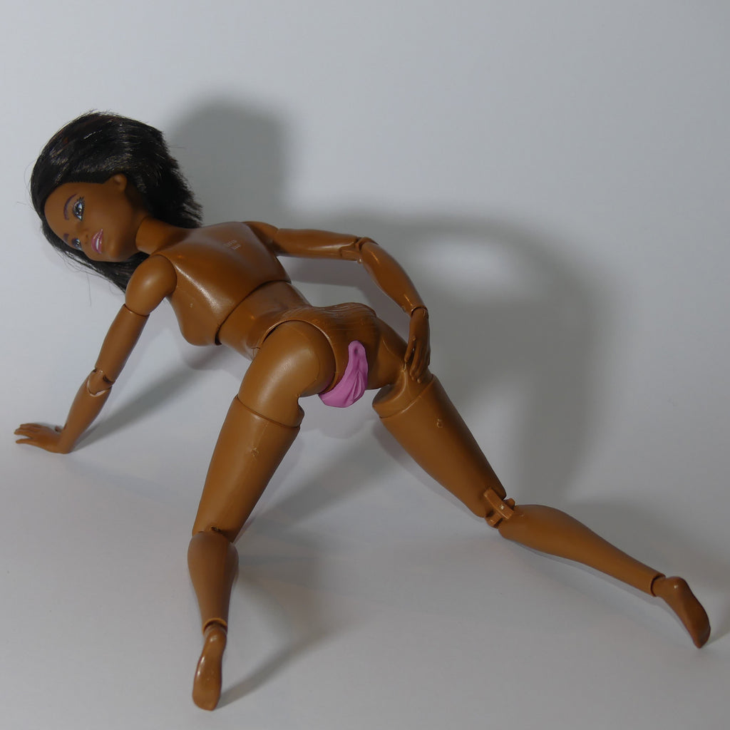 A brown articulated doll posed on a light gray background, wearing a small pink barbie vagina under the hips.