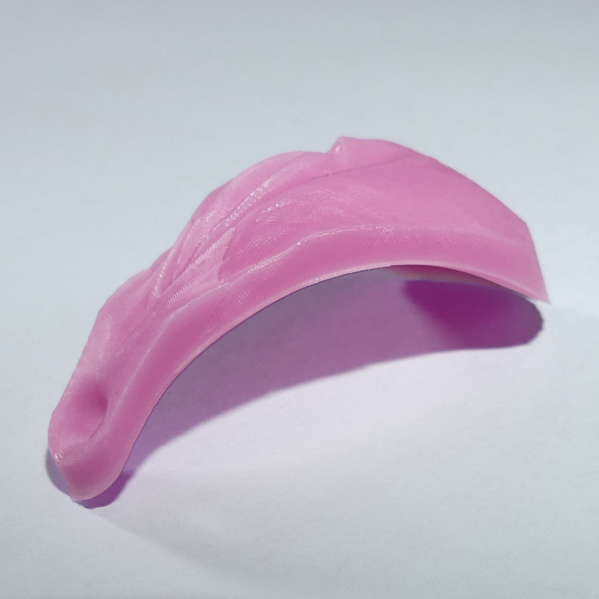 A pink vagina vulva curved silicone or rubber accessory with a textured surface and a small anal, shown on a plain light gray background.